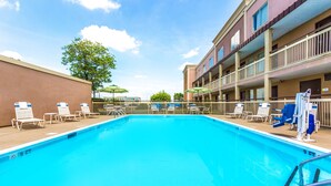 A swimming pool with lounge chairs and umbrellas, surrounded by a building with balconies and a tree. - Days Inn by Wyndham Florence Cincinnati Area (Florence)
