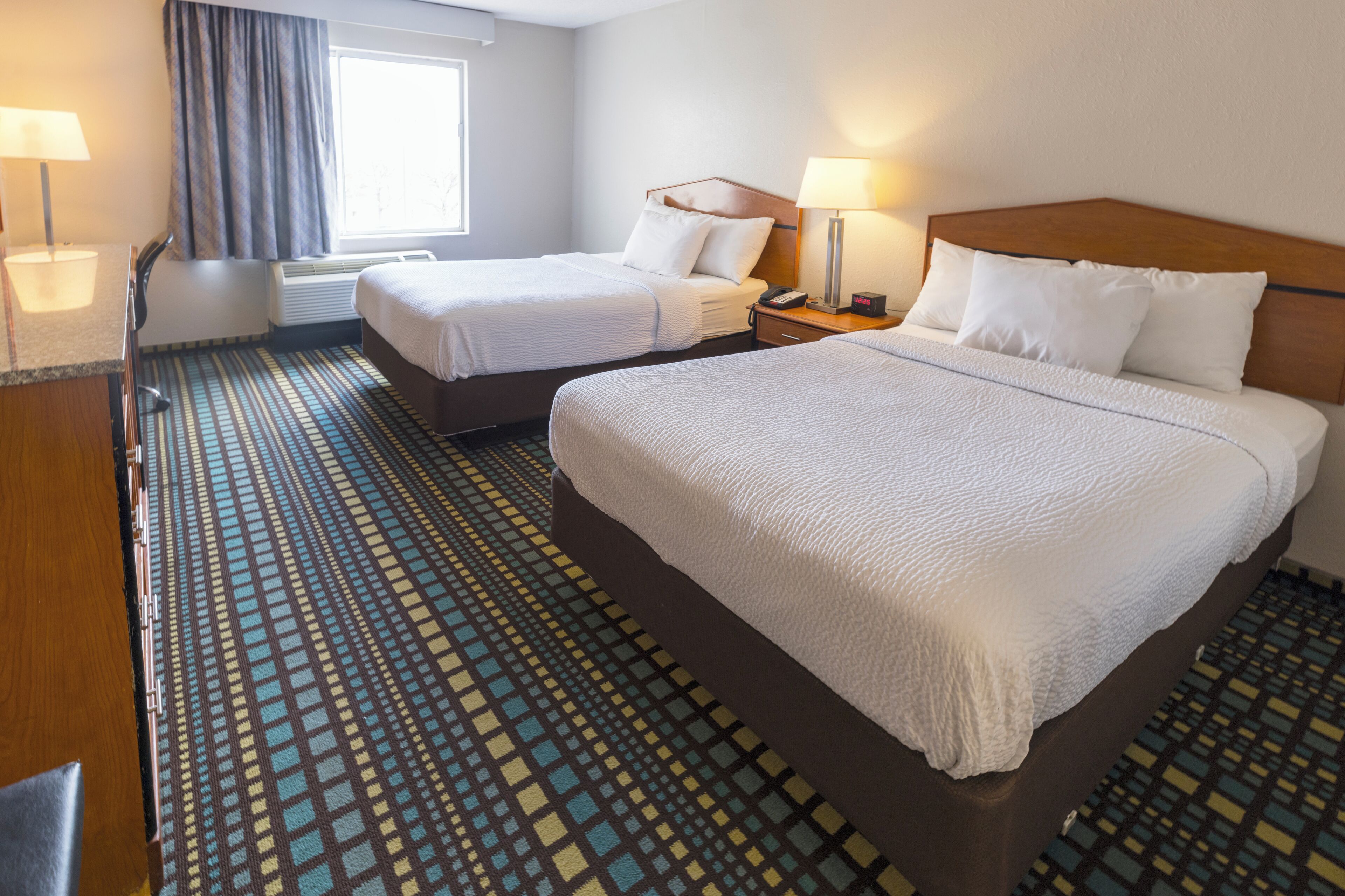 A hotel room with two beds, a desk, a chair, and a window with curtains.