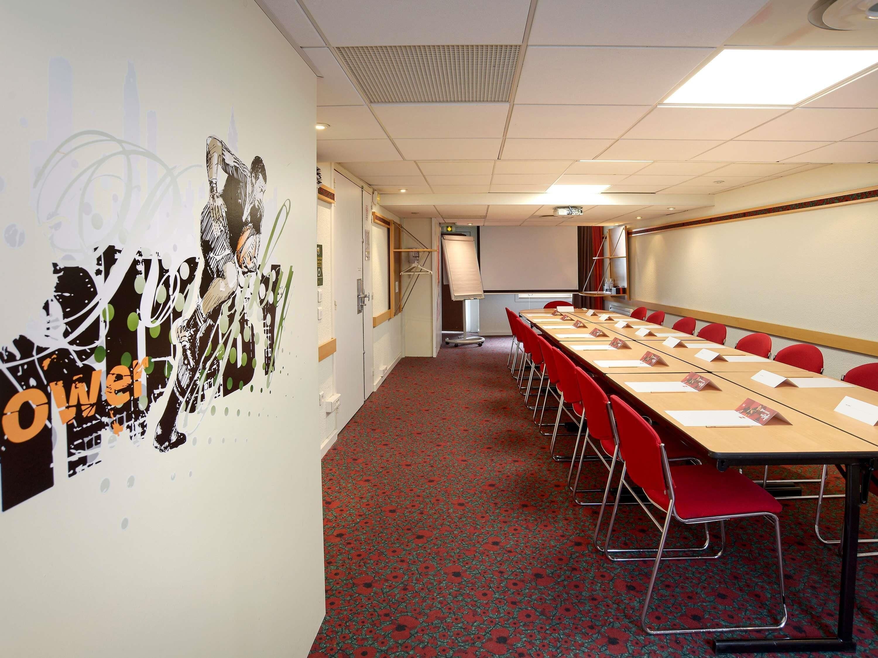 A conference room with a long table, red chairs, a projector screen, and a whiteboard.