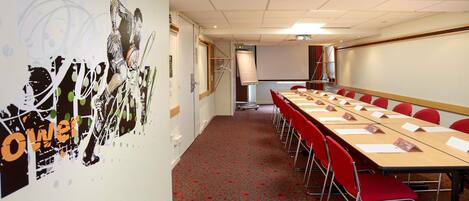 A conference room with a long table, red chairs, a projector screen, and a whiteboard.