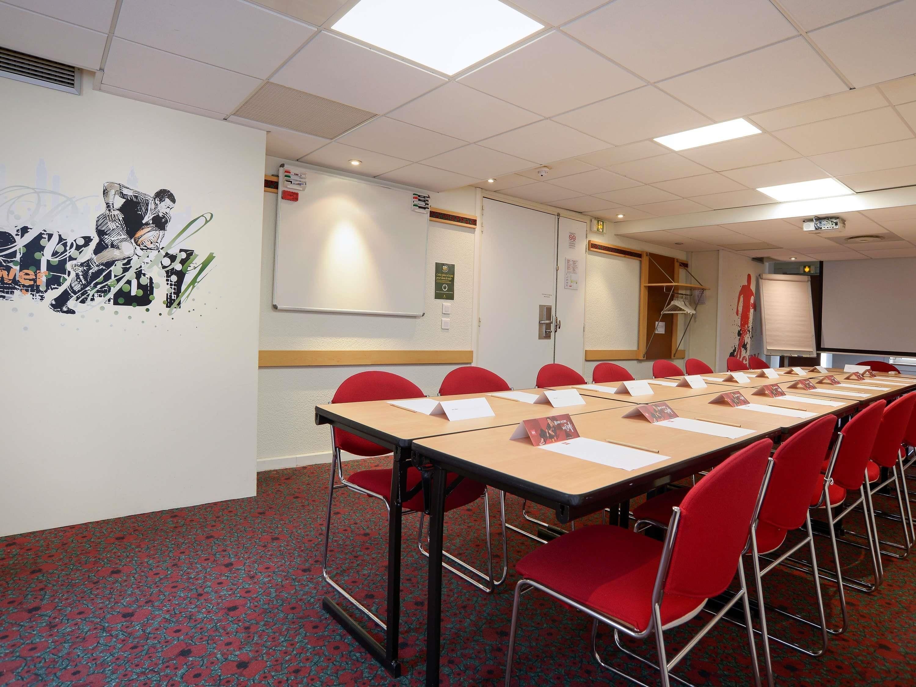 A conference room with a long table, red chairs, a whiteboard, and a projector screen.
