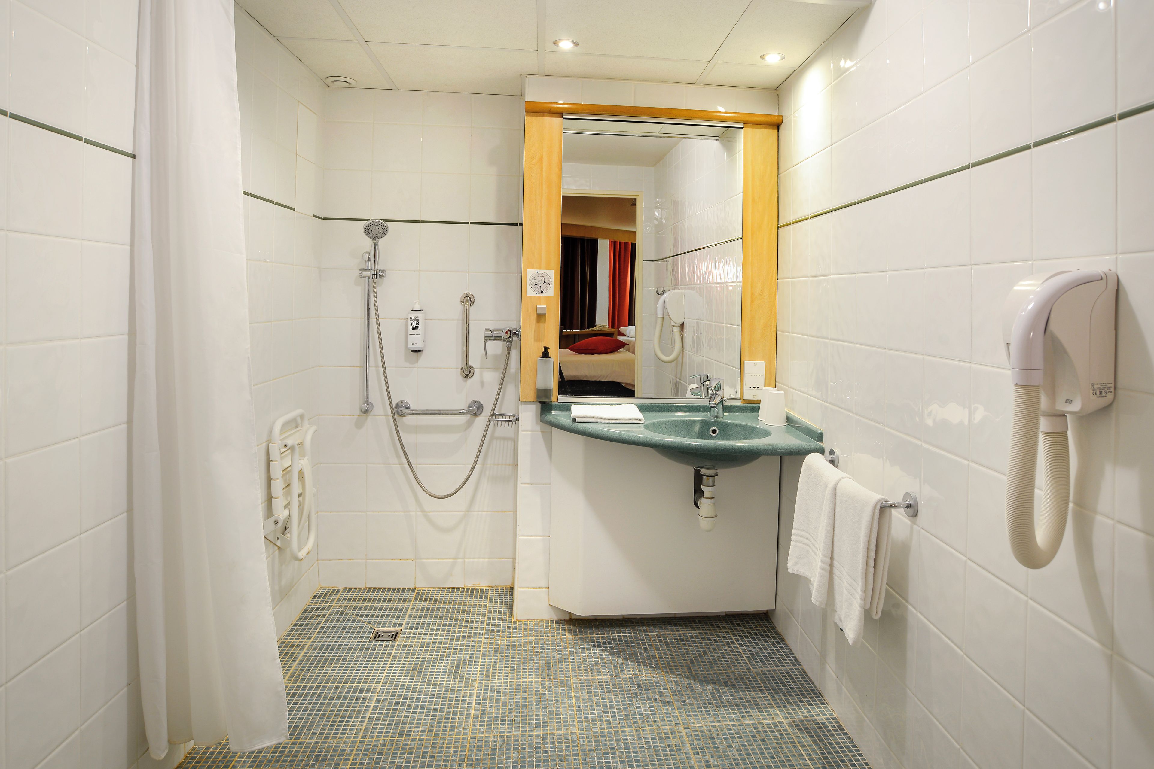A small bathroom with a shower, a sink, and a mirror.