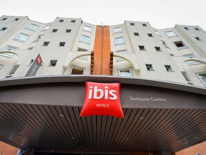 Ein Hotel mit einem auffälligen roten 'ibis'-Schild, einem modernen architektonischen Design und dem Schriftzug 'Toulouse Centre' an der Fassade.