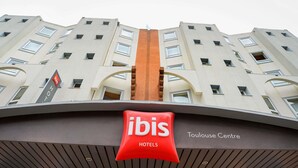 A hotel with a prominent red ibis logo, a modern architectural design with a central vertical element, and the name 'Toulouse Centre' on the facade.