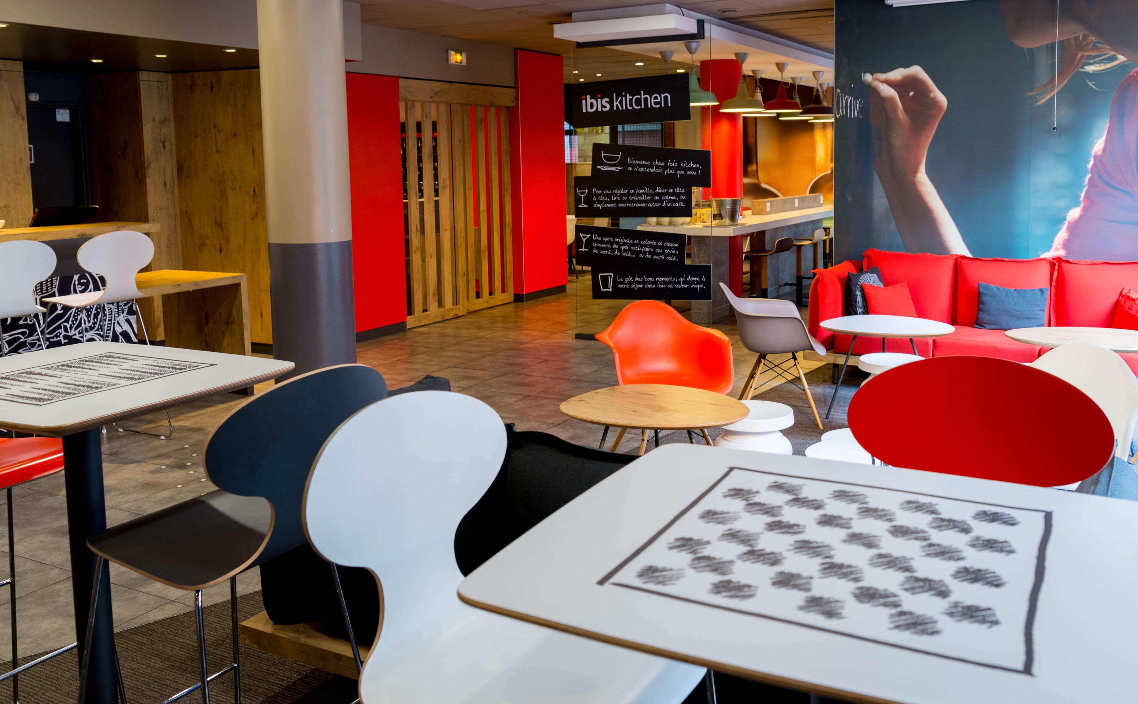 A modern restaurant interior with red and white seating, a blackboard with writing, and a sign reading "ibis kitchen".