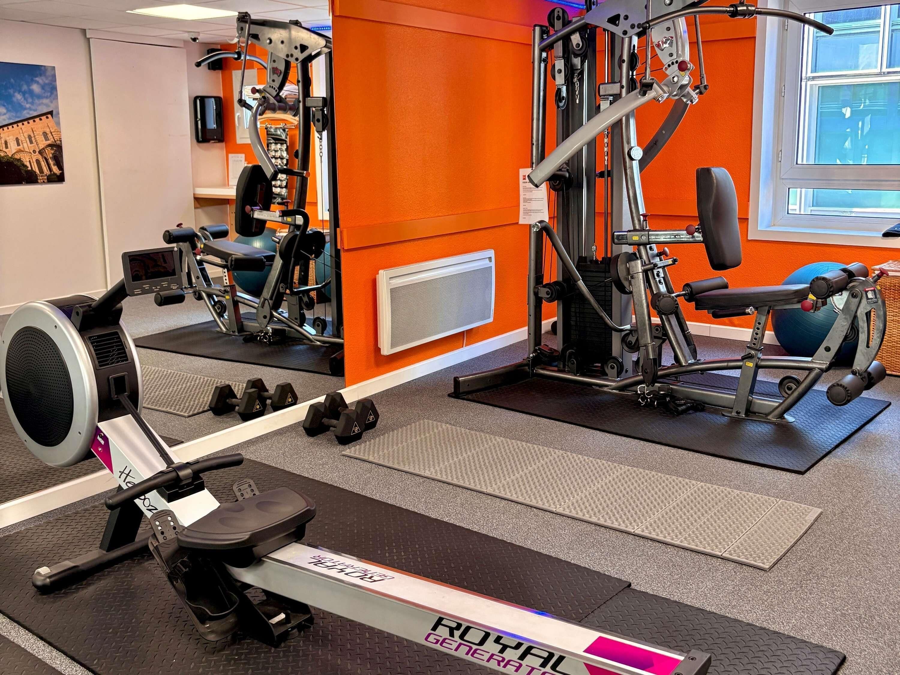 A gym with exercise equipment, a rowing machine, and dumbbells.
