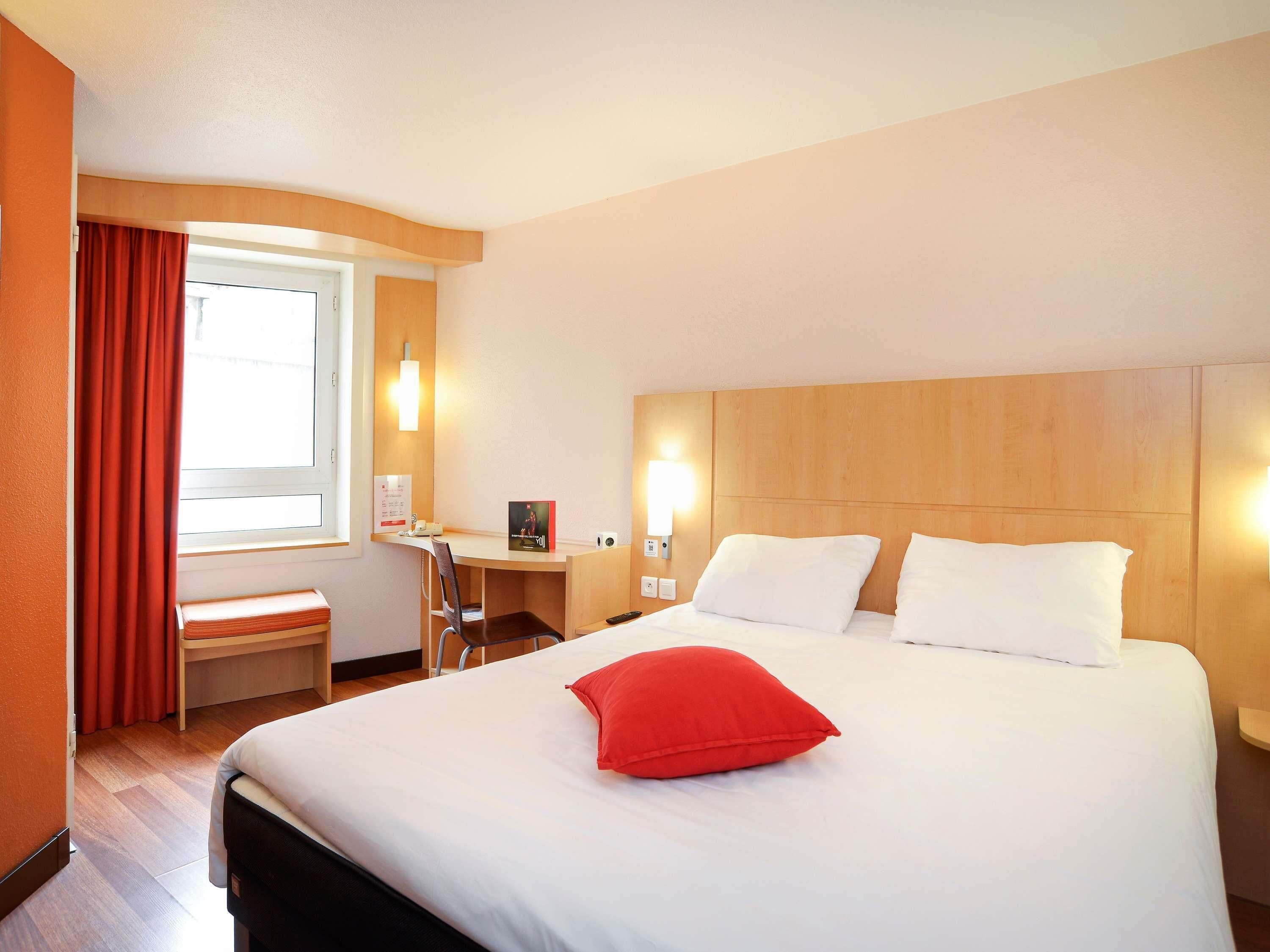A hotel room with a bed, a desk, a chair, and a window with curtains.