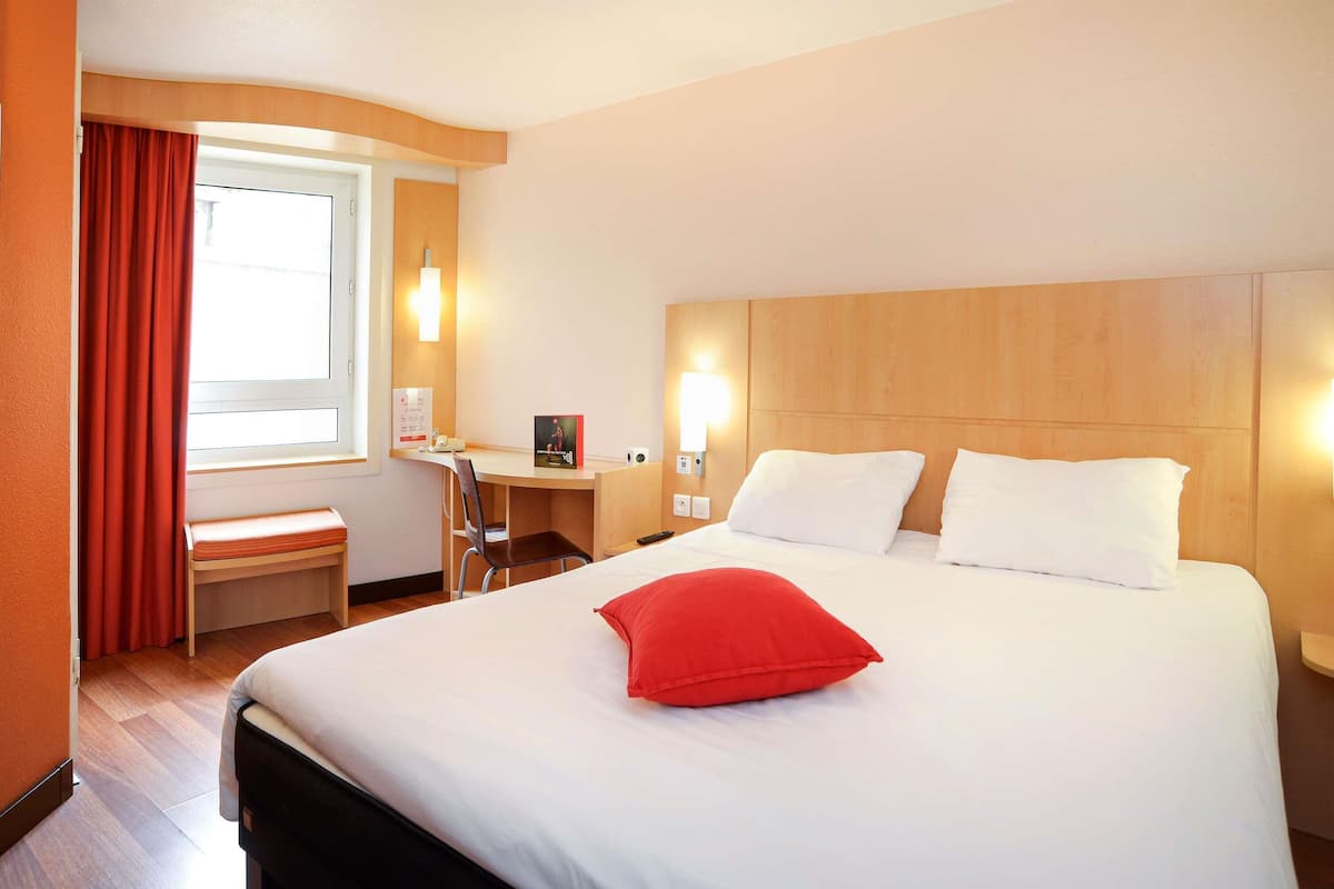 A hotel room with a bed, a desk, a chair, and a window with curtains.