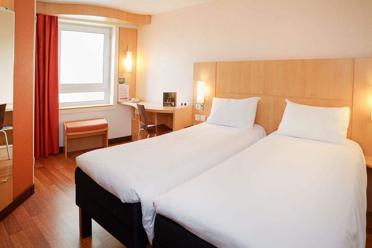 A hotel room with two beds, a desk, a chair, and a window with curtains.