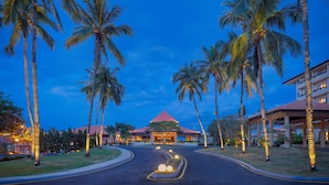 Un resort con un edificio central, palmeras y un camino bien iluminado.