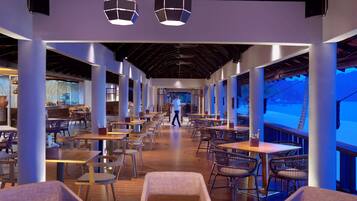 A spacious restaurant with high ceilings, modern lighting, and a view of the beach.