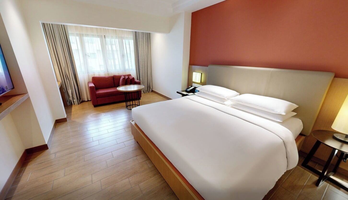 Una habitación de hotel con una cama grande, un sillón rojo, una mesita redonda y un escritorio con una lámpara.