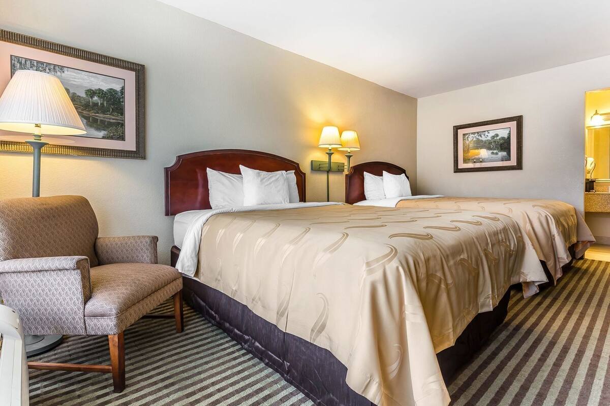 Una habitación de hotel con cama, una silla, una lámpara y dos lámparas fijadas a la pared.
