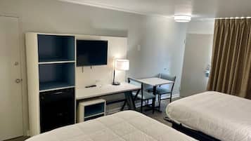 Habitación de hotel con dos camas, un escritorio, una silla, un televisor y una lámpara.