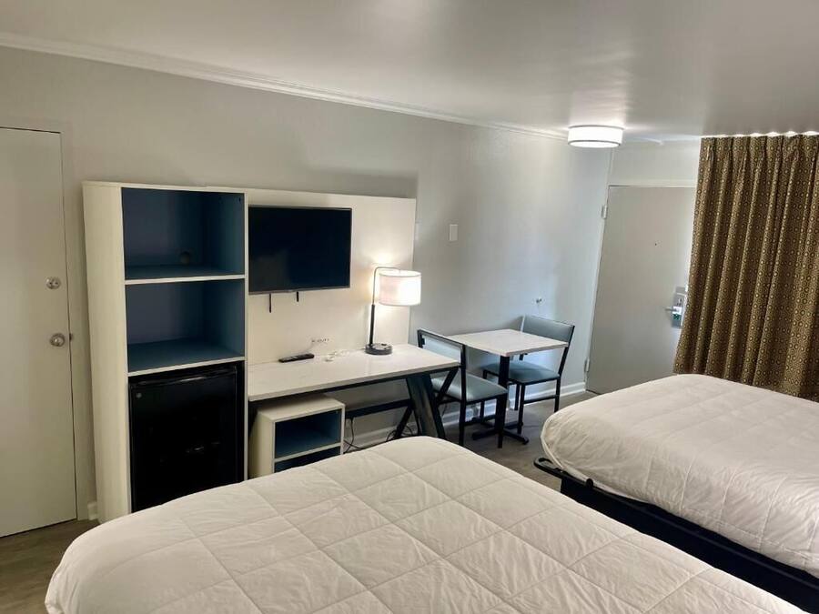 Habitación de hotel con dos camas, un escritorio, una silla, un televisor y una lámpara.
