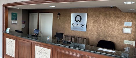 A hotel reception desk with a 'Quality by Choice Hotels' sign, a 'Manager on Duty' sign, and a security camera.