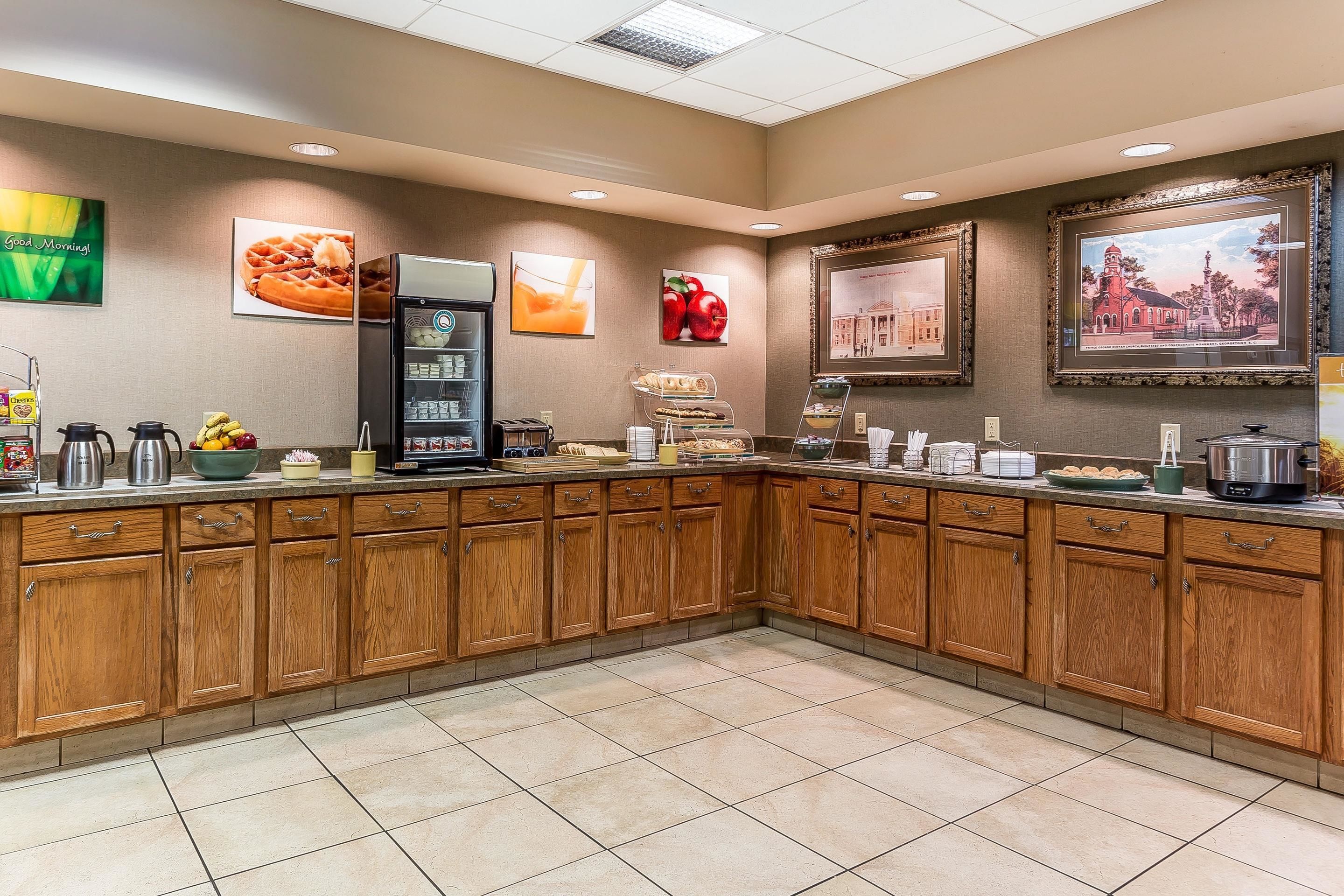 A hotel kitchen with wooden cabinets, a coffee machine, and various food items on the counter.