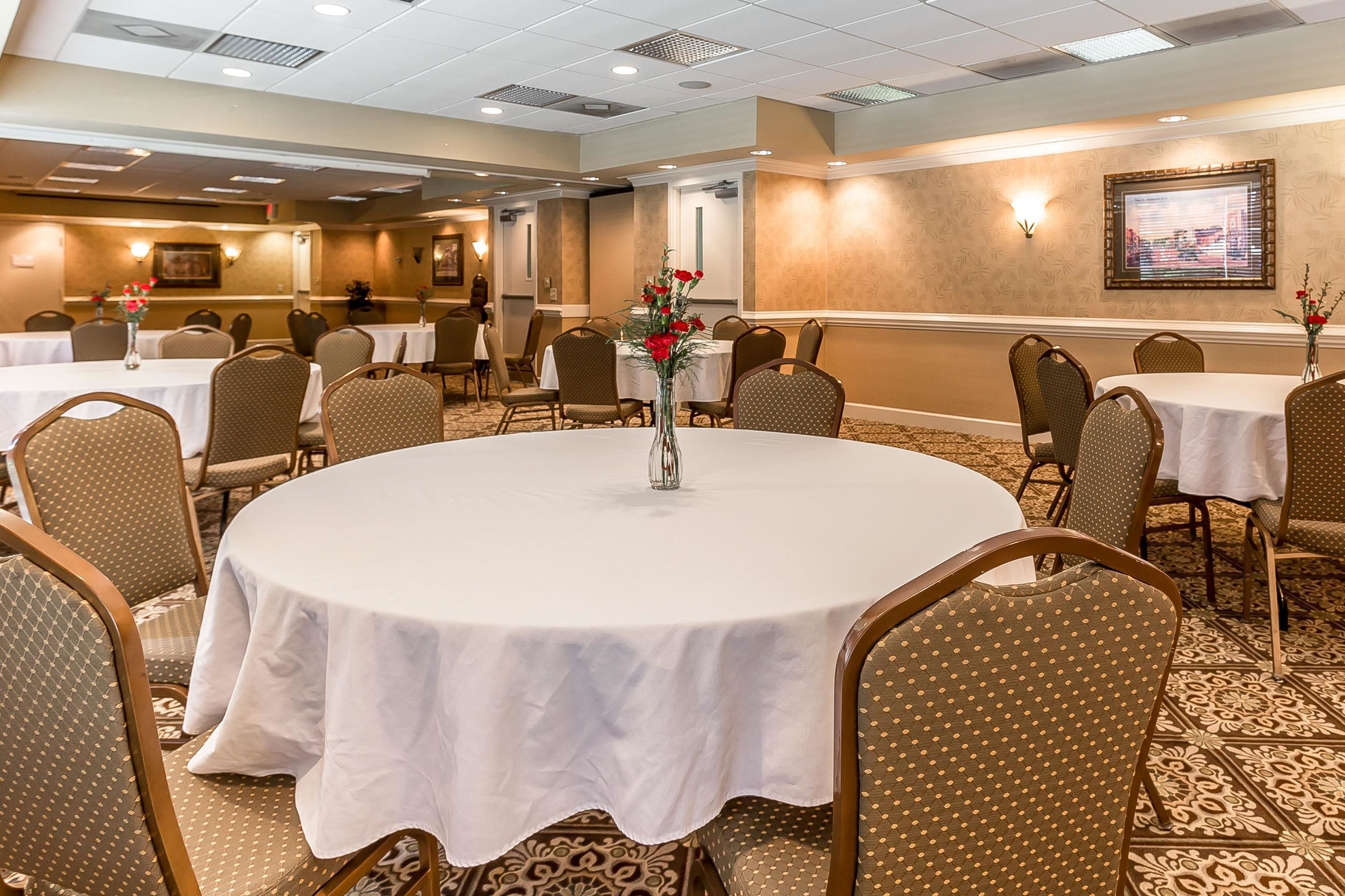 Un salón de conferencias con mesas redondas, sillas y un centro de mesa con flores.