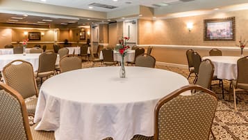 Un salón de conferencias con mesas redondas, sillas y un centro de mesa con flores.