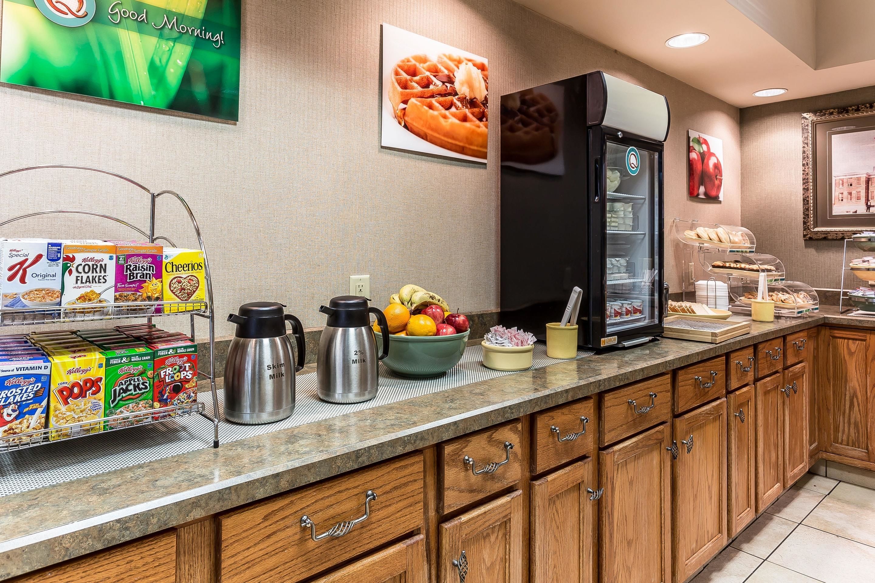 A hotel kitchen with cereal boxes, a fruit bowl, a coffee maker, and a refrigerator.