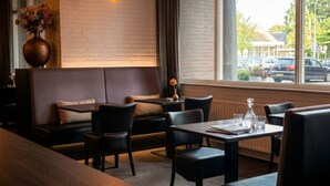 A restaurant interior with a brick wall, a sofa, dining tables, and chairs. - A-Hotel Oosterhout (Oosterhout)