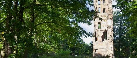 A historic stone tower with multiple arched windows, surrounded by lush green trees and grass.