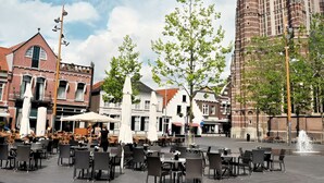 A square with outdoor seating, a tall brick building, and a fountain. - A-Hotel Oosterhout (Oosterhout)