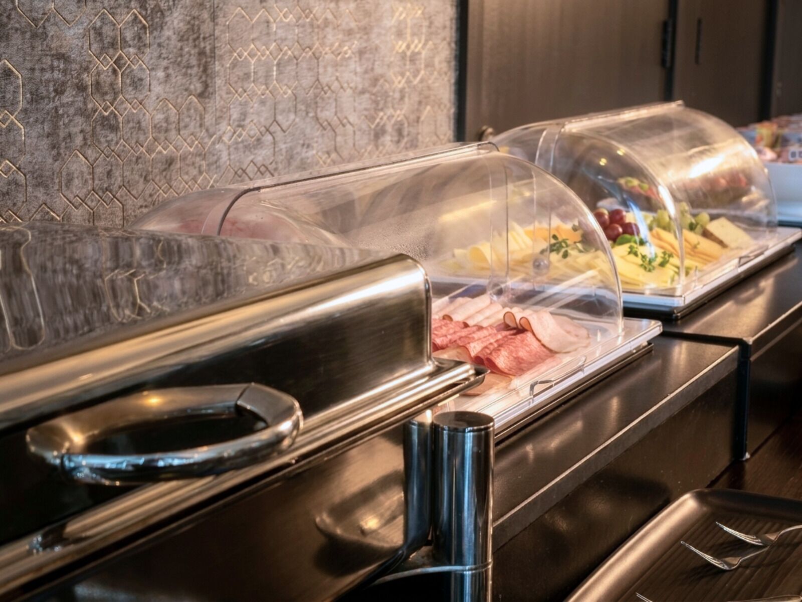 A buffet with various food items under clear plastic covers.