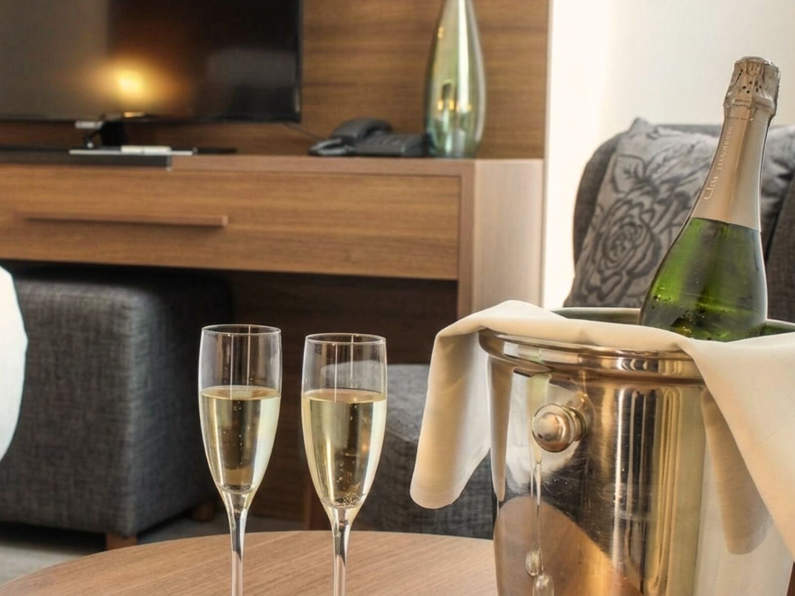 Una habitación con una mesa de madera, dos copas de vino blanco y una botella de champán en un balde de metal.