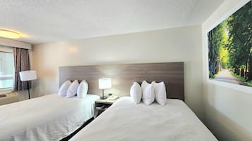 A hotel room with two beds, a nightstand with a lamp, a painting of a forest, and a window with curtains.