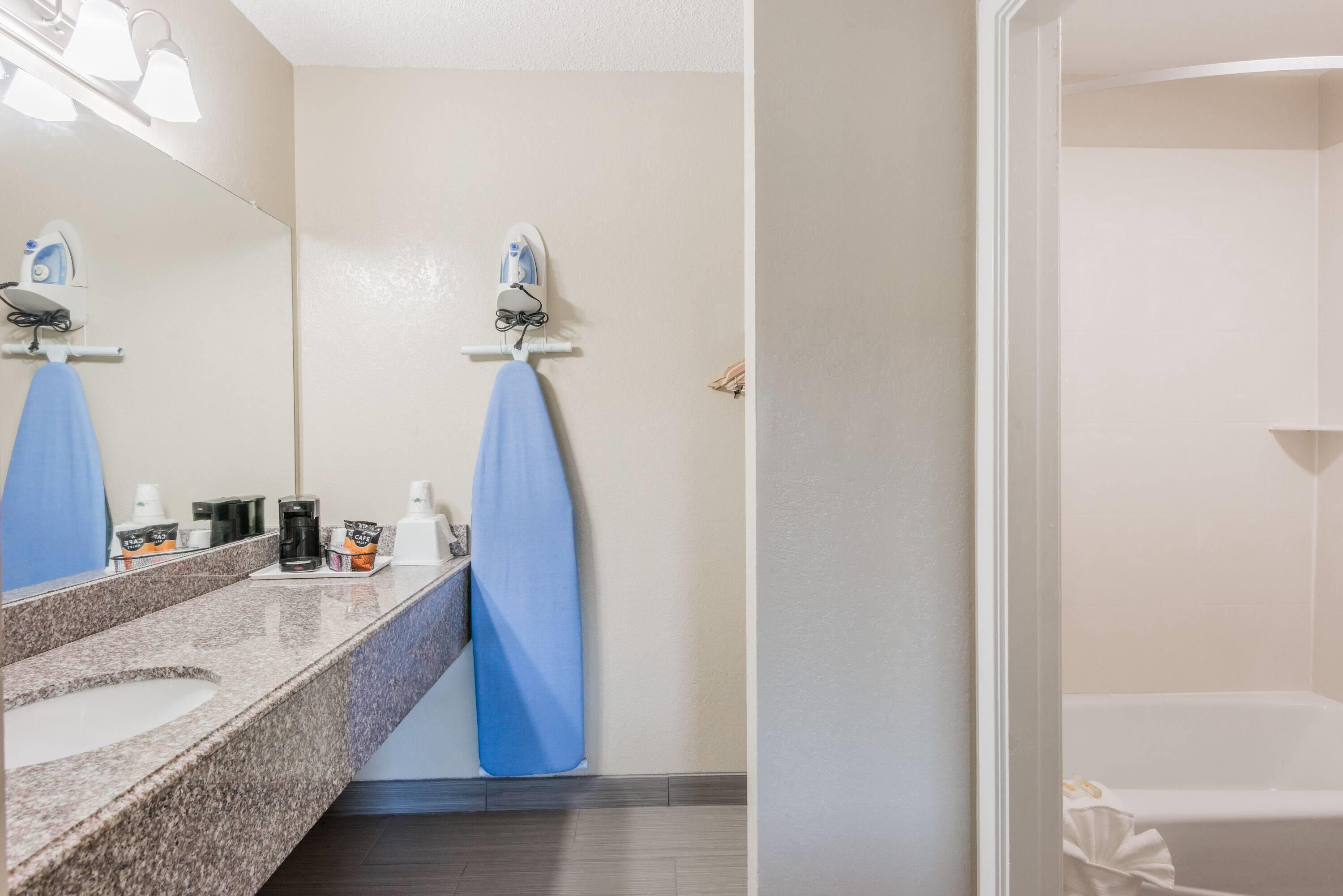 A bathroom with a granite countertop, a mirror, a towel rack with a blue towel, and a white bathtub.