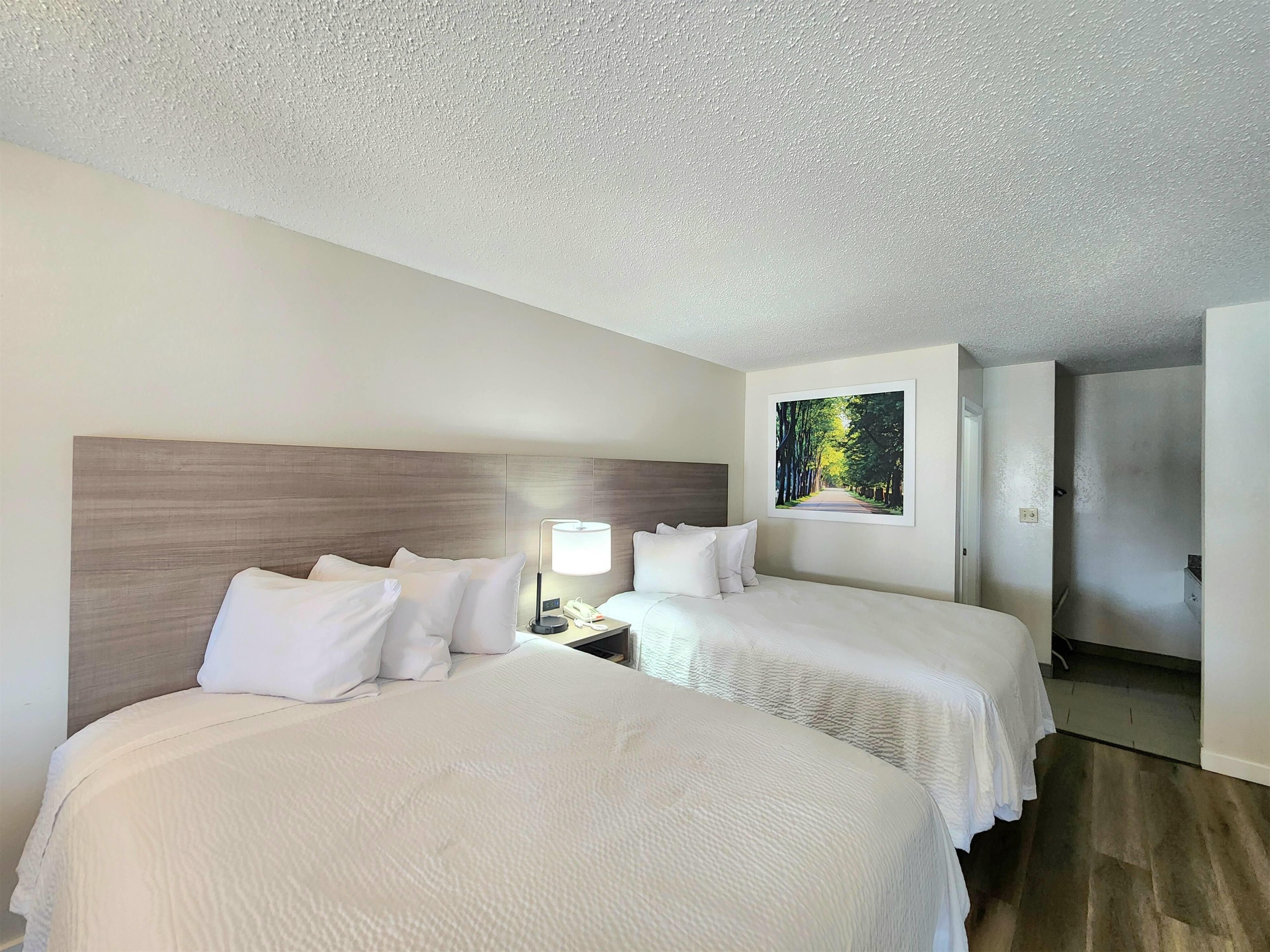 Ein Hotelzimmer mit zwei Betten, einem Nachttisch mit Lampe und einem Bild an der Wand.