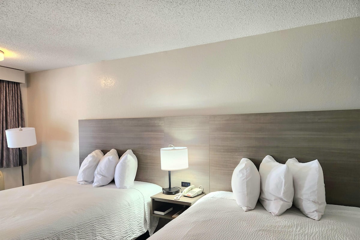 A hotel room with two beds, a nightstand with a lamp, and a telephone.
