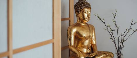 Uma estátua dourada de Buda sentado em um pedestal, acompanhado por um vaso com galhos.