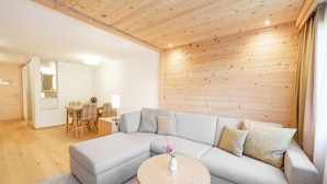 A modern living room with a sectional sofa, a round coffee table, and a dining area with a table and chairs. - Gstaaderhof – Active & Relax Hotel  (Saanen)