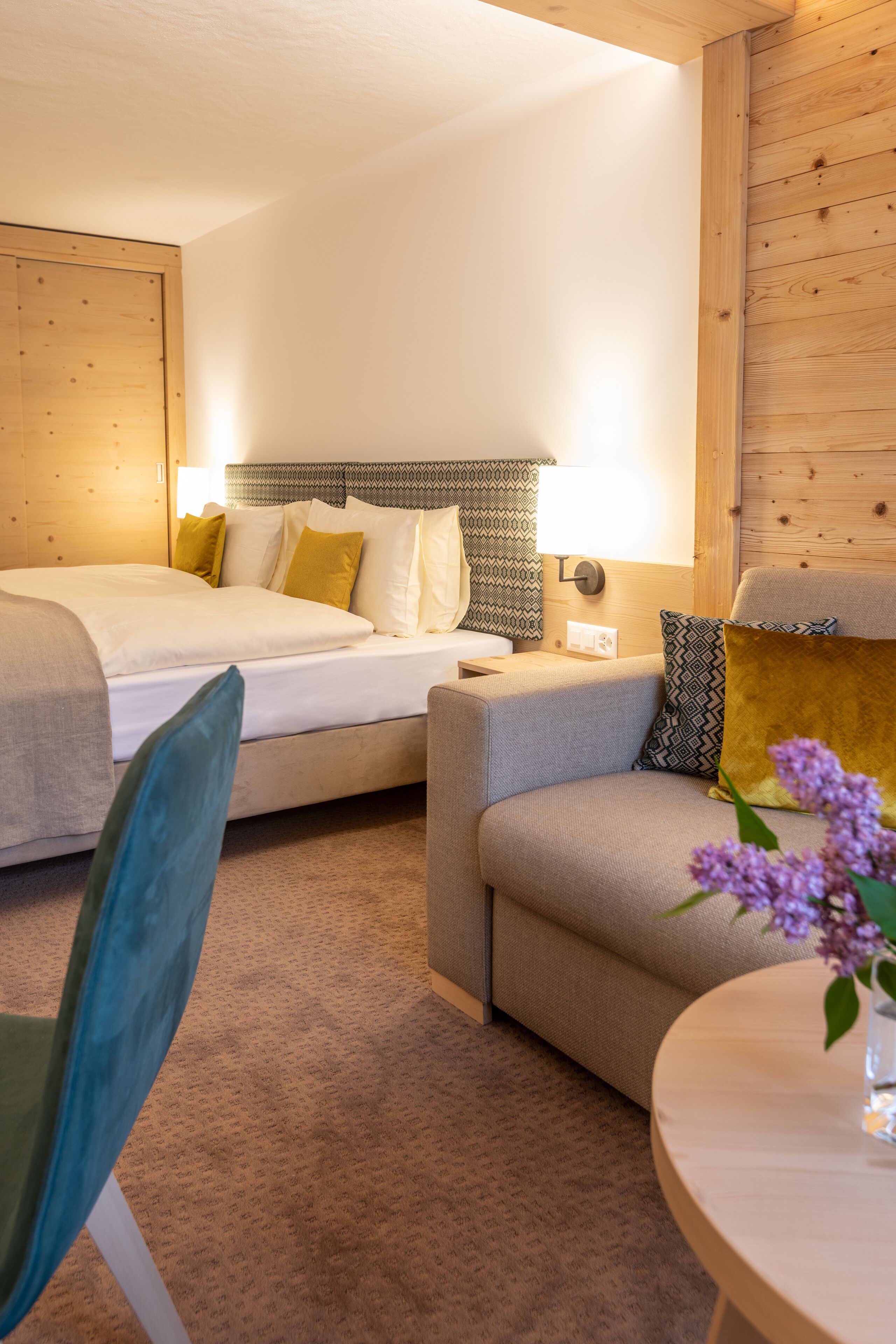 Habitación de hotel con dos camas, un sofá, una silla y una mesita con un jarrón de flores.