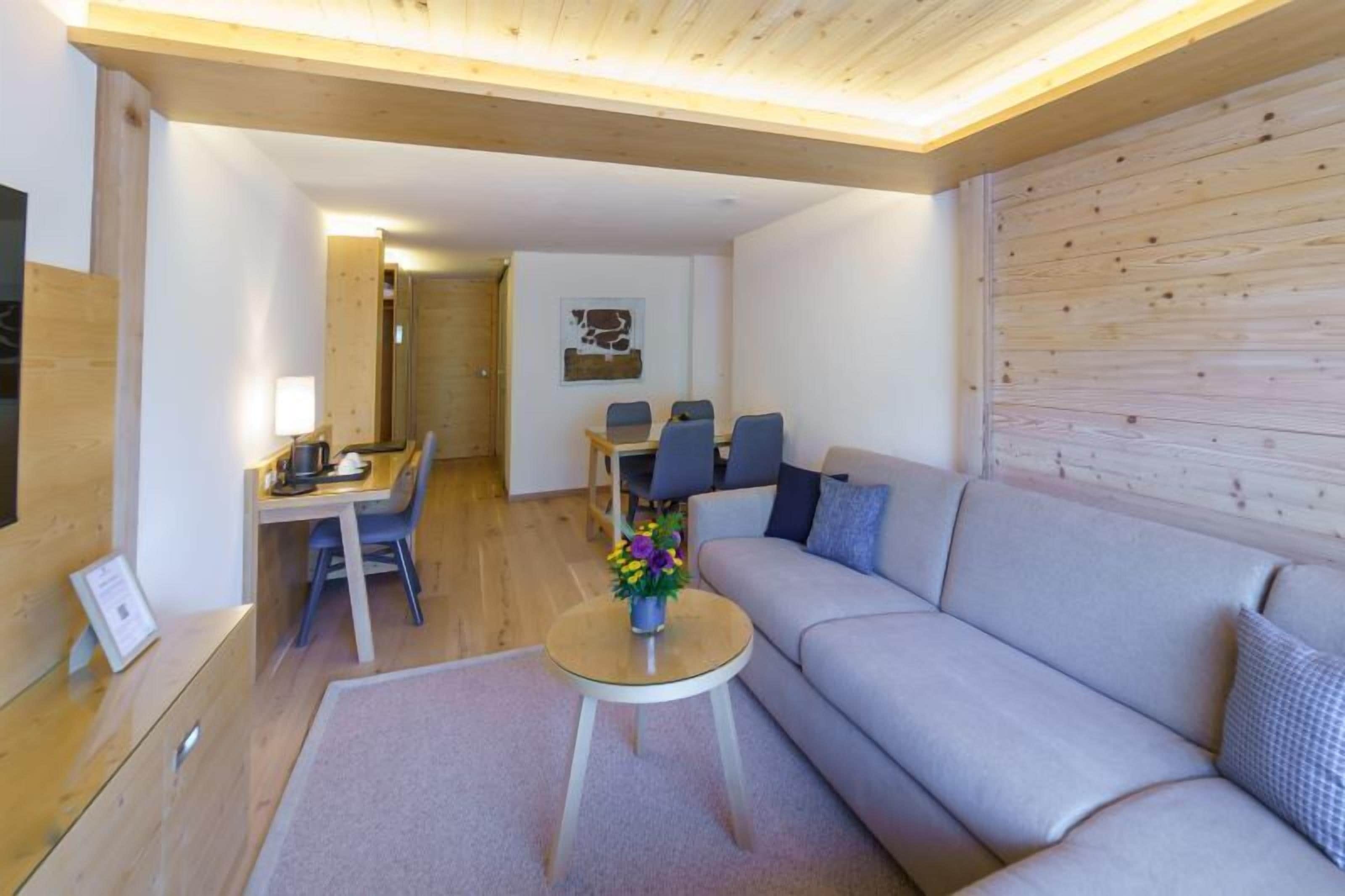 En moderne stue med en sofa, et sofabord med blomster, et spiseområde med stole og et træloft.