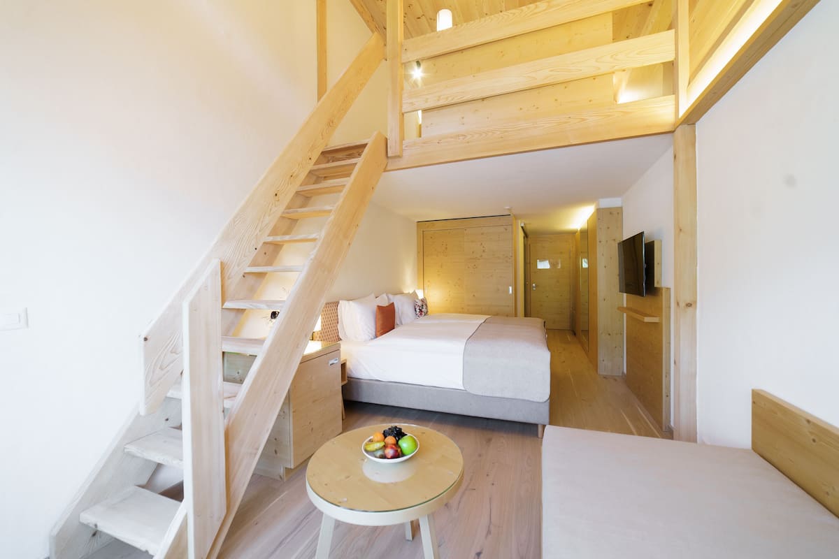 Une chambre avec un lit, une petite table sur laquelle se trouvent des fruits, un escalier en bois et un téléviseur.