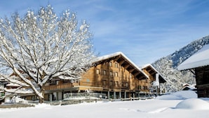 A wooden building with a sloped roof, labeled "Gstaadhof," surrounded by snow-covered trees and a clear sky. - Gstaaderhof – Active & Relax Hotel  (Saanen)