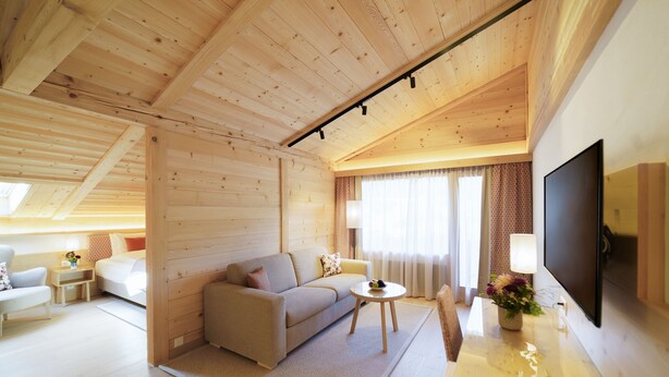 A modern log cabin with a wooden interior, a sofa, a coffee table, a TV, and a desk with a lamp.