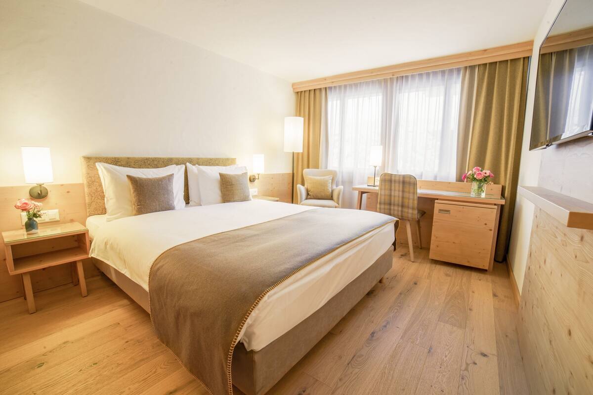 Hotellihuone, jossa on suuri sänky, yöpöydät, työpöytä, tuoli ja pieni kaappi.
