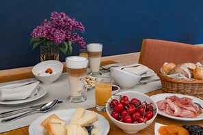 Une table mise pour le petit-déjeuner, avec divers aliments, un vase de fleurs et un verre de jus d’orange.