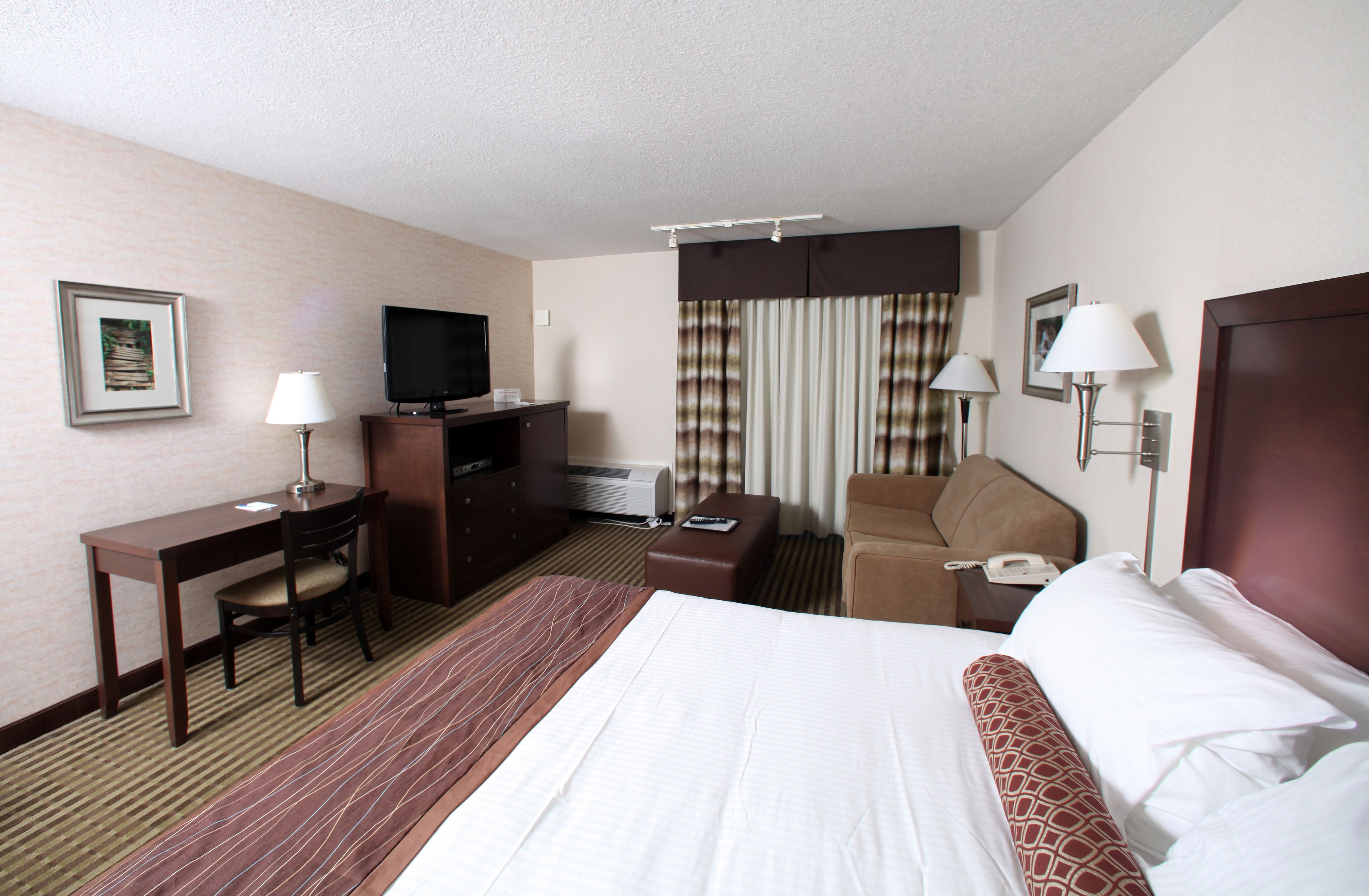 A hotel room with a bed, desk, chair, television, and a telephone.