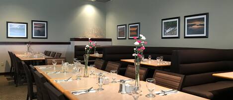 A restaurant with long wooden tables, cushioned booths, and framed pictures on the walls.
