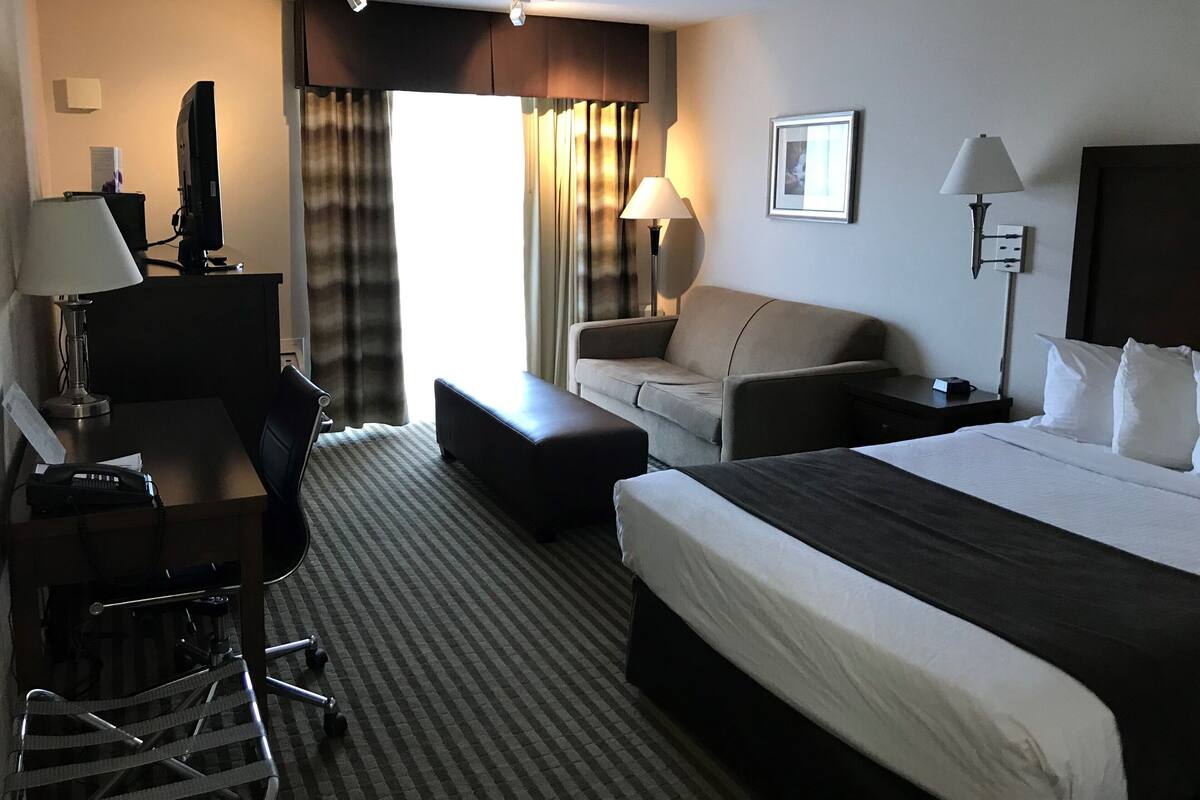 A hotel room with a bed, a desk, a chair, a sofa, and a TV.