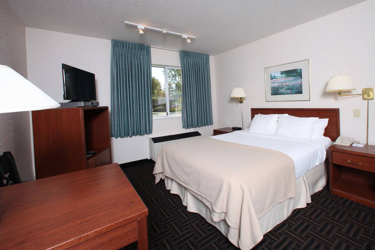 A hotel room with a bed, bedside tables, a desk, a television, and a window with curtains.
