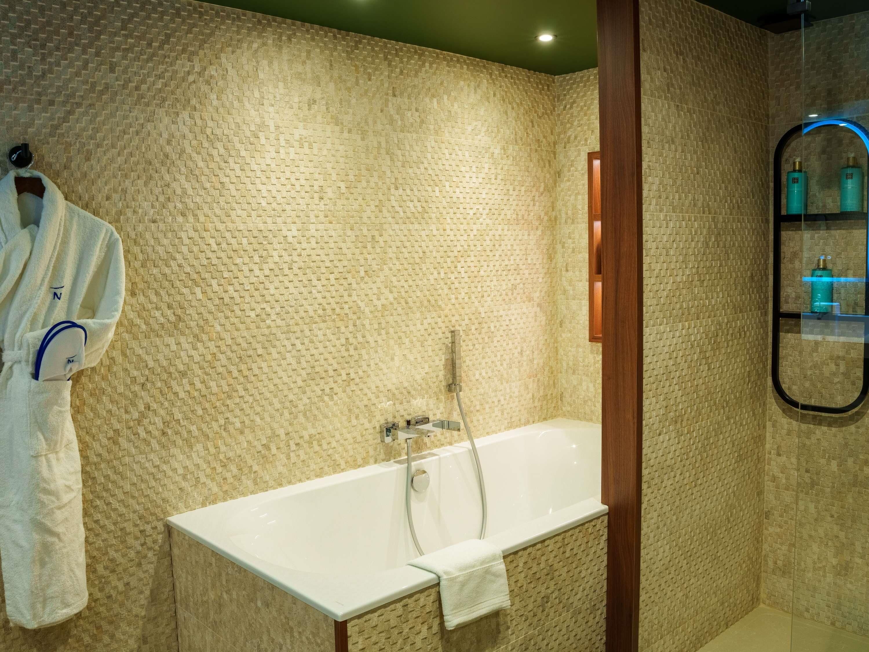Un baño con pared texturizada, una bañera, un perchero para toallas y un espejo con marco de madera.