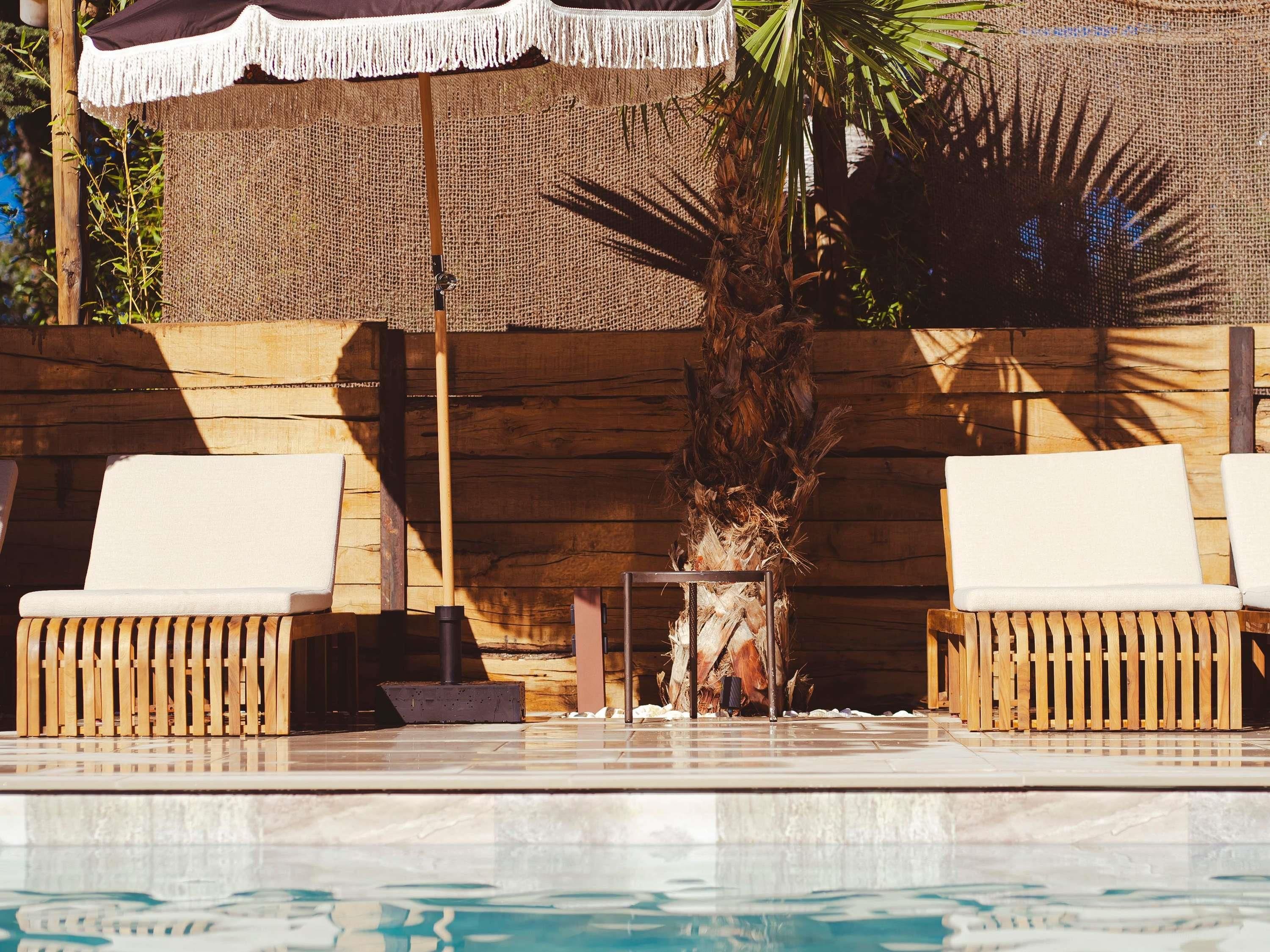 A poolside area with two wicker lounge chairs, a small table, and a palm tree.