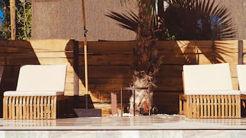 A poolside area with two wicker lounge chairs, a small table, and a palm tree.
