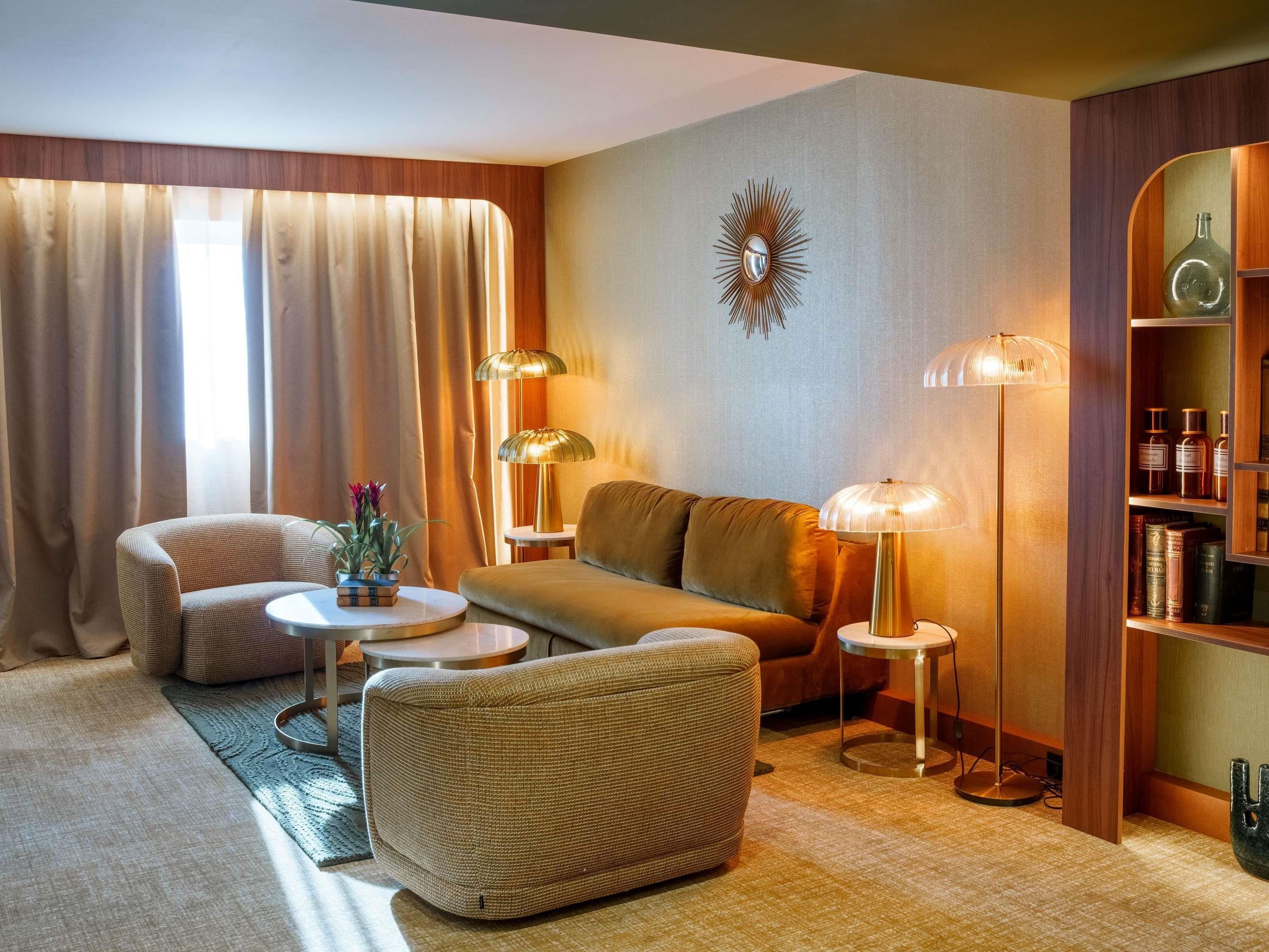 Een gezellige woonkamer met een bank, fauteuil en twee bijzettafels, een boekenkast vol boeken en een decoratief wandobject.